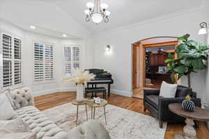 Living area with arched walkways, vaulted ceiling, wood finished floors, a notable chandelier, and ornamental molding
