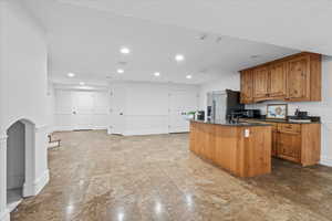 Kitchen featuring stainless steel fridge, brown cabinetry, a kitchen island with sink, and recessed lighting
