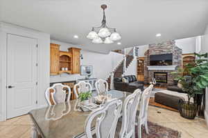 Dining area with stairs, a chandelier, a stone fireplace, and light tile patterned floors