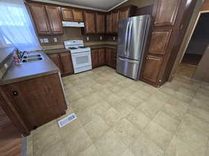 Kitchen featuring a sink, white gas range, freestanding refrigerator, under cabinet range hood, and visible vents