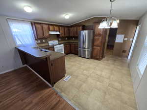 Kitchen with freestanding refrigerator, a peninsula, white range with gas stovetop, under cabinet range hood, and vaulted ceiling