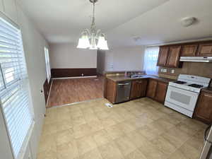 Kitchen with stainless steel dishwasher, an inviting chandelier, a sink, dark countertops, and white gas range oven