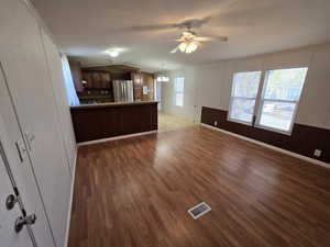 Unfurnished living room with vaulted ceiling, ceiling fan with notable chandelier, wood finished floors, and visible vents