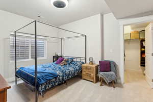 Bedroom featuring a walk in closet, visible vents, and light colored carpet
