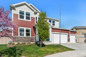 View of front of property with fence, stone siding, a front yard, board and batten siding, and concrete driveway