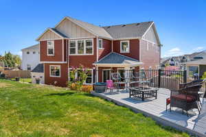 Back of property featuring a shingled roof, board and batten siding, a deck, a yard, and a fire pit