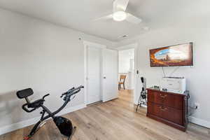 Workout area featuring a ceiling fan, baseboards, visible vents, and light wood finished floors