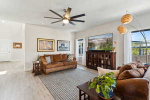 Living room with light wood-type flooring, a ceiling fan, and baseboards