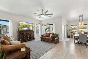 Living area with light wood-style flooring, a wealth of natural light, and ceiling fan with notable chandelier