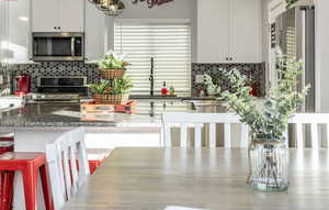 Modern kitchen featuring a healthy amount of sunlight, walk-in pantry, large island with seating for eight+, stainless steel appliances, white shaker cabinetry, undermount black granite kitchen sink, beautiful hexagon backsplash, recessed lighting, custom