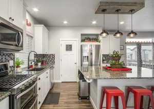 Modern kitchen featuring a healthy amount of sunlight, walk-in pantry, large island with seating for eight+, stainless steel appliances, white shaker cabinetry, undermount black granite kitchen sink, beautiful hexagon backsplash, recessed lighting, custom