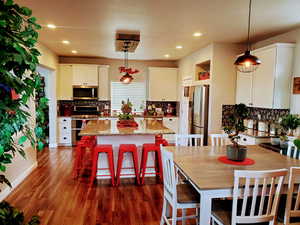 Modern kitchen featuring a healthy amount of sunlight, walk-in pantry, large island with seating for eight+, stainless steel appliances, white shaker cabinetry, undermount black granite kitchen sink, beautiful hexagon backsplash, recessed lighting, custom