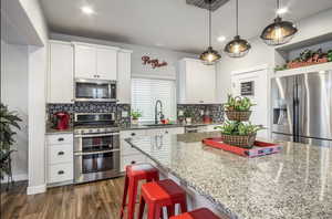 Modern kitchen featuring a healthy amount of sunlight, walk-in pantry, large island with seating for eight+, stainless steel appliances, white shaker cabinetry, undermount black granite kitchen sink, beautiful hexagon backsplash, recessed lighting, custom