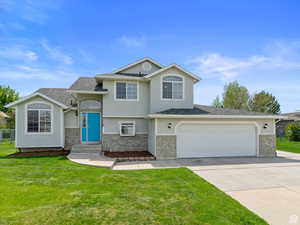 Split level home featuring brick siding, driveway, a front yard, and stucco siding