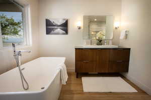 Full bath with double vanity, baseboards, wood finished floors, and a freestanding tub