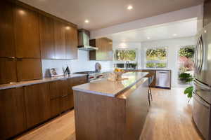 Kitchen with wall chimney range hood, modern cabinets, stainless steel appliances, and light wood finished floors
