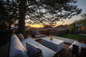 Patio terrace at dusk featuring an outdoor living space, fence, a yard, and a deck
