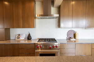 Kitchen featuring light stone countertops, stainless steel stove, modern cabinets, wall chimney exhaust hood, and backsplash