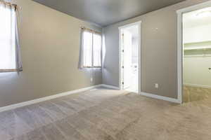 Unfurnished bedroom featuring a walk in closet, baseboards, a closet, connected bathroom, and carpet