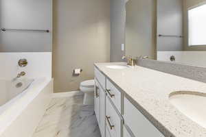 Full bathroom featuring marble finish floor, toilet, baseboards, a bath, and a sink