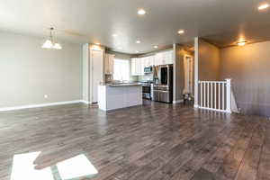 Unfurnished living room featuring dark wood-type flooring, recessed lighting, baseboards, and an inviting chandelier