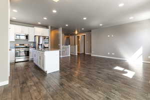 Kitchen with appliances with stainless steel finishes, white cabinetry, open floor plan, dark wood-type flooring, and a kitchen island