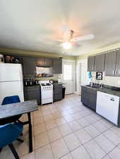 Kitchen with ceiling fan, dark countertops, light tile floors, a garden sink, and white appliances