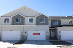 View of property with board and batten siding, driveway, stone siding, and a garage
