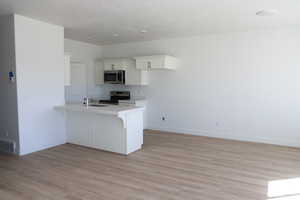 Kitchen featuring appliances with stainless steel finishes, light countertops, white cabinets, a peninsula, and a breakfast bar