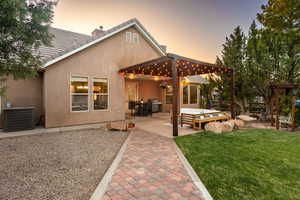 Back of property at dusk featuring central AC, stucco siding, outdoor lounge area, a lawn, and a patio