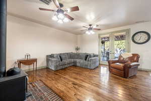 Living area with a wood stove, french doors, a ceiling fan, visible vents, and hardwood / wood-style flooring