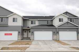 View of property featuring board and batten siding, an attached garage, driveway, and stone siding