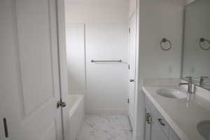 Full bath featuring a sink, double vanity, marble finish floor, baseboards, and a bath