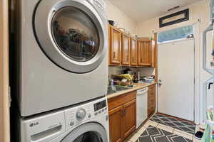Washroom featuring stacked washer and dryer, a sink, light tile patterned floors, visible vents, and ornamental molding