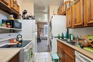 Kitchen with visible vents, stacked washer / dryer, white appliances, brown cabinets, and a sink