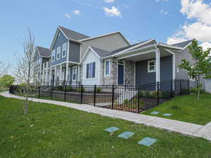 View of front facade featuring covered porch, a fenced front yard, stone siding, and a front yard
