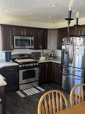 Kitchen featuring a textured ceiling, dark brown cabinetry, dark wood-style floors, and stainless steel appliances