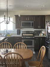 Kitchen featuring dark wood-style flooring, a textured ceiling, a sink, a chandelier, and stainless steel appliances