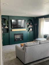Living room with a textured ceiling, a fireplace, and built in shelves