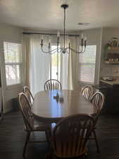 Dining area with a chandelier, a textured ceiling, visible vents, and dark wood-type flooring