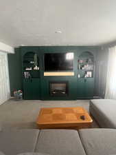 Carpeted living room with a textured ceiling, built in features, and a fireplace