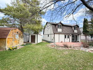 Rear view of house featuring a gambrel roof, a patio area, a shed, a lawn, and roof with shingles