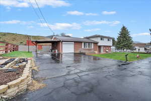 Tri-level home featuring fence, aphalt driveway, brick siding, an attached carport, and a front yard