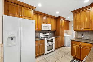 Kitchen with decorative backsplash, brown cabinets, white appliances, and washing machine and clothes dryer