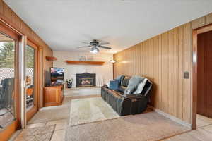 Living area featuring wooden walls, a ceiling fan, a textured ceiling, and a fireplace