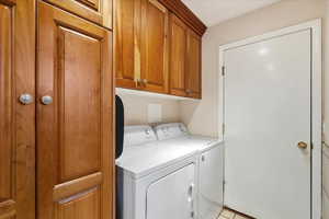 Laundry area featuring independent washer and dryer, light tile patterned floors, and cabinet space