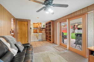 Living room with visible vents, wood walls, light carpet, a textured ceiling, and a ceiling fan