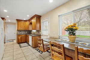 Kitchen with decorative backsplash, white dishwasher, brown cabinets, a sink, and light tile patterned floors