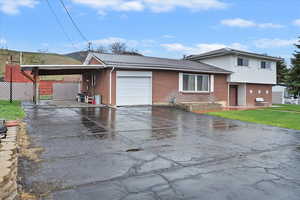Tri-level home with driveway, metal roof, brick siding, an attached garage, and an attached carport
