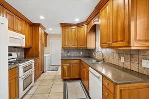 Kitchen with white appliances, brown cabinets, washer and clothes dryer, and a sink